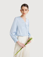 a lady in a light blue silk woven blouse with white pants